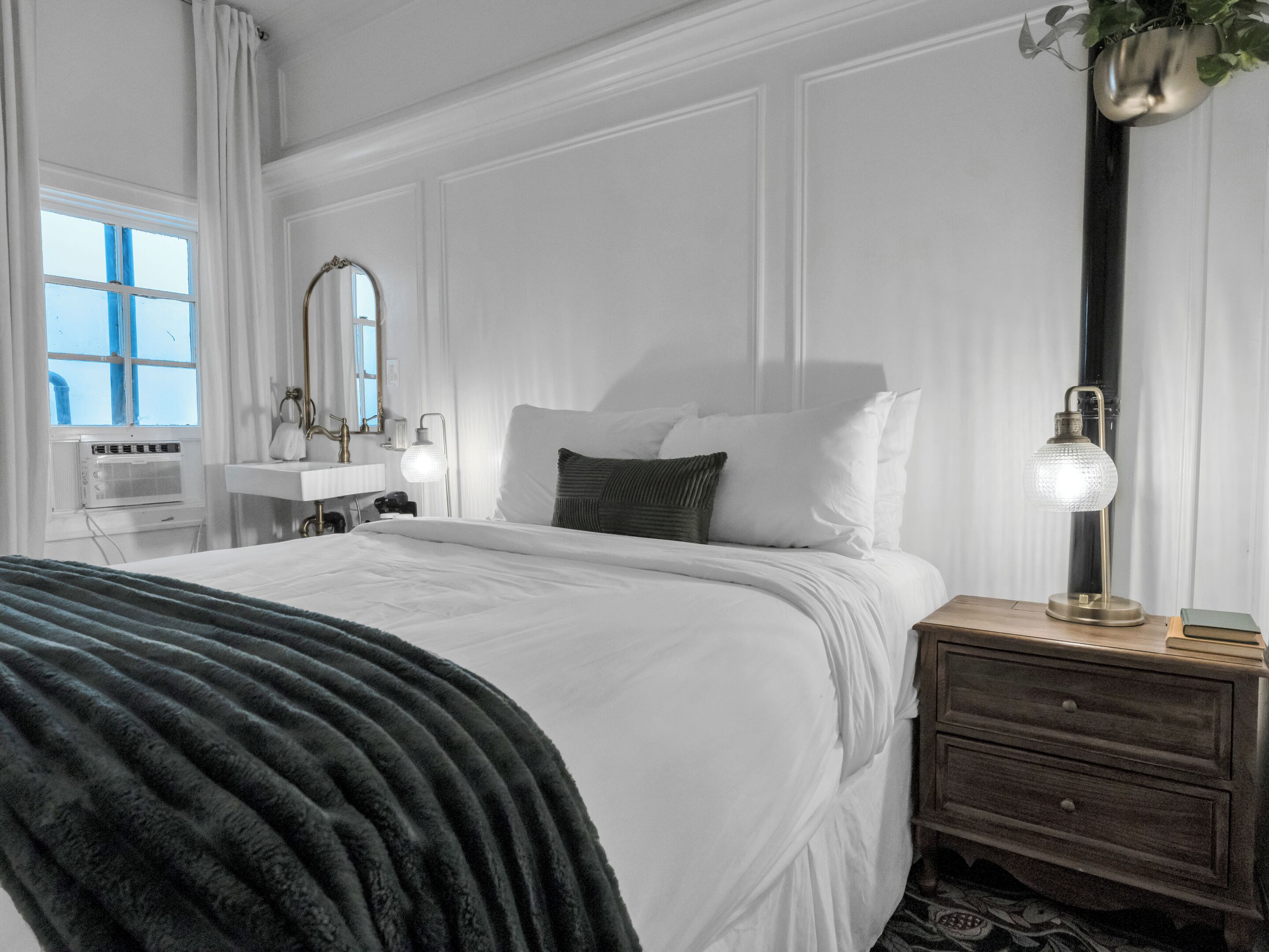 A neatly arranged bedroom with a bed, bedside tables, a mirror, and a lamp.