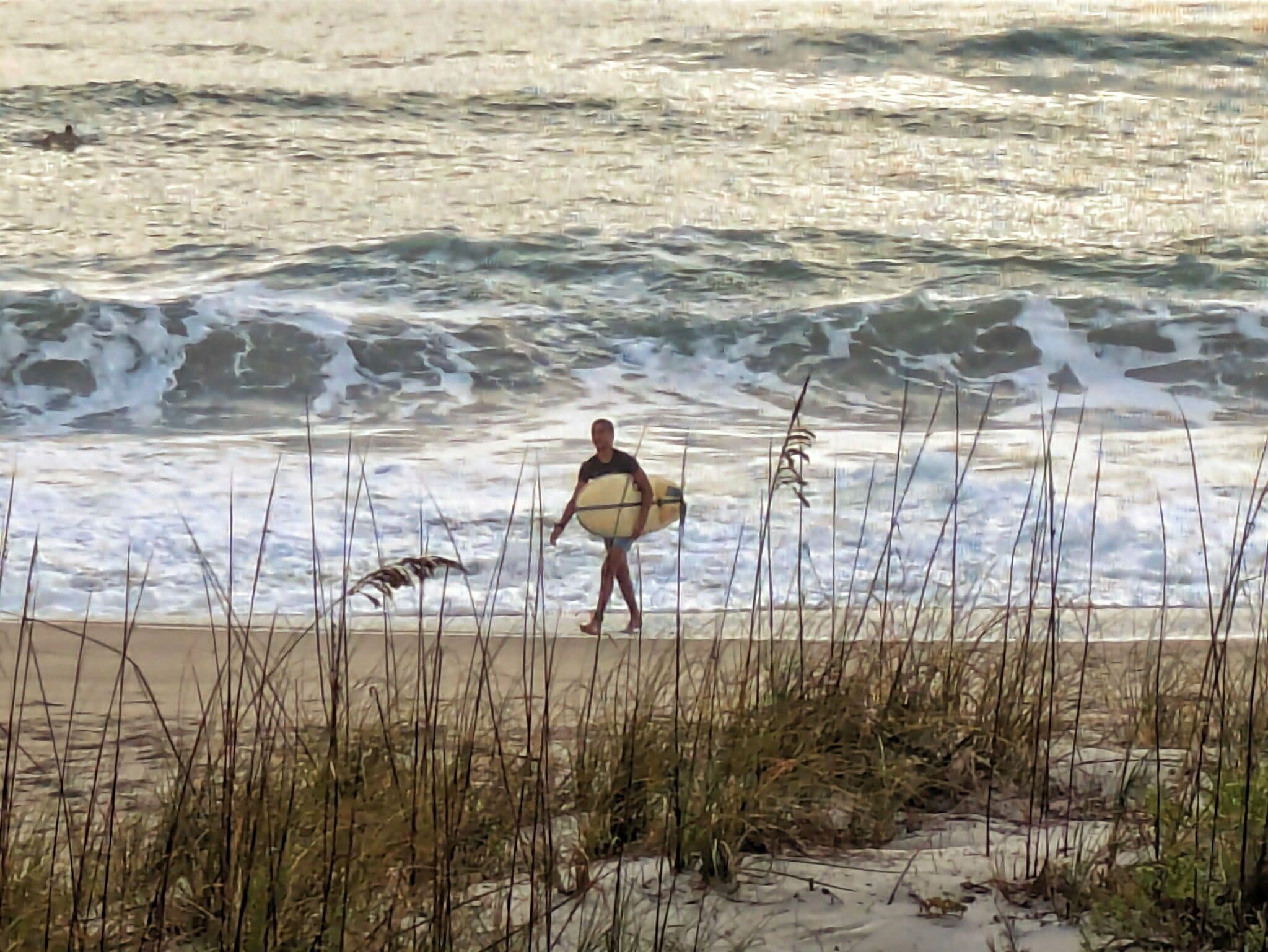 Una persona lleva una tabla de surf por la playa, con olas.