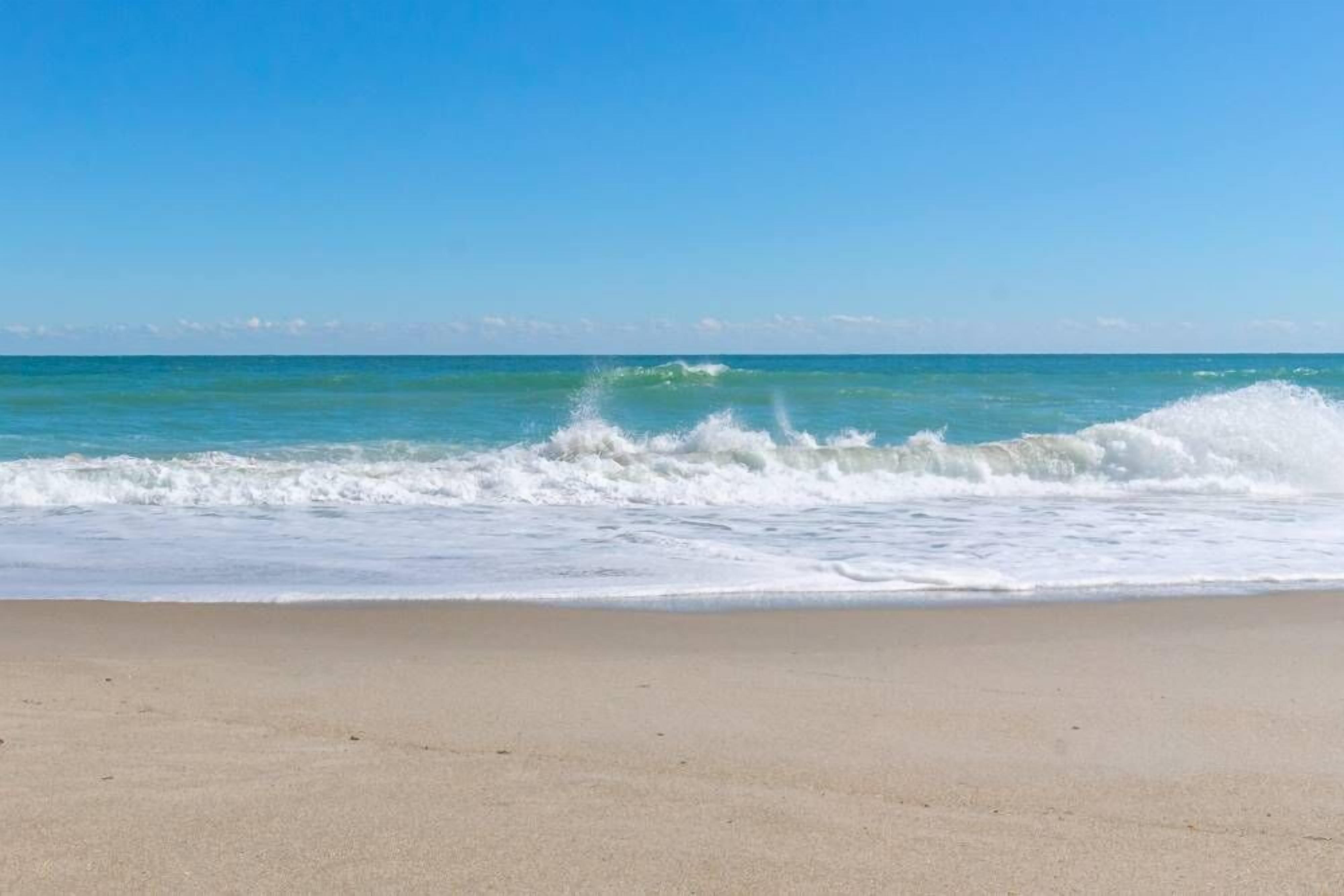 Una platja amb onades que trenquen a la riba sota un cel serè.
