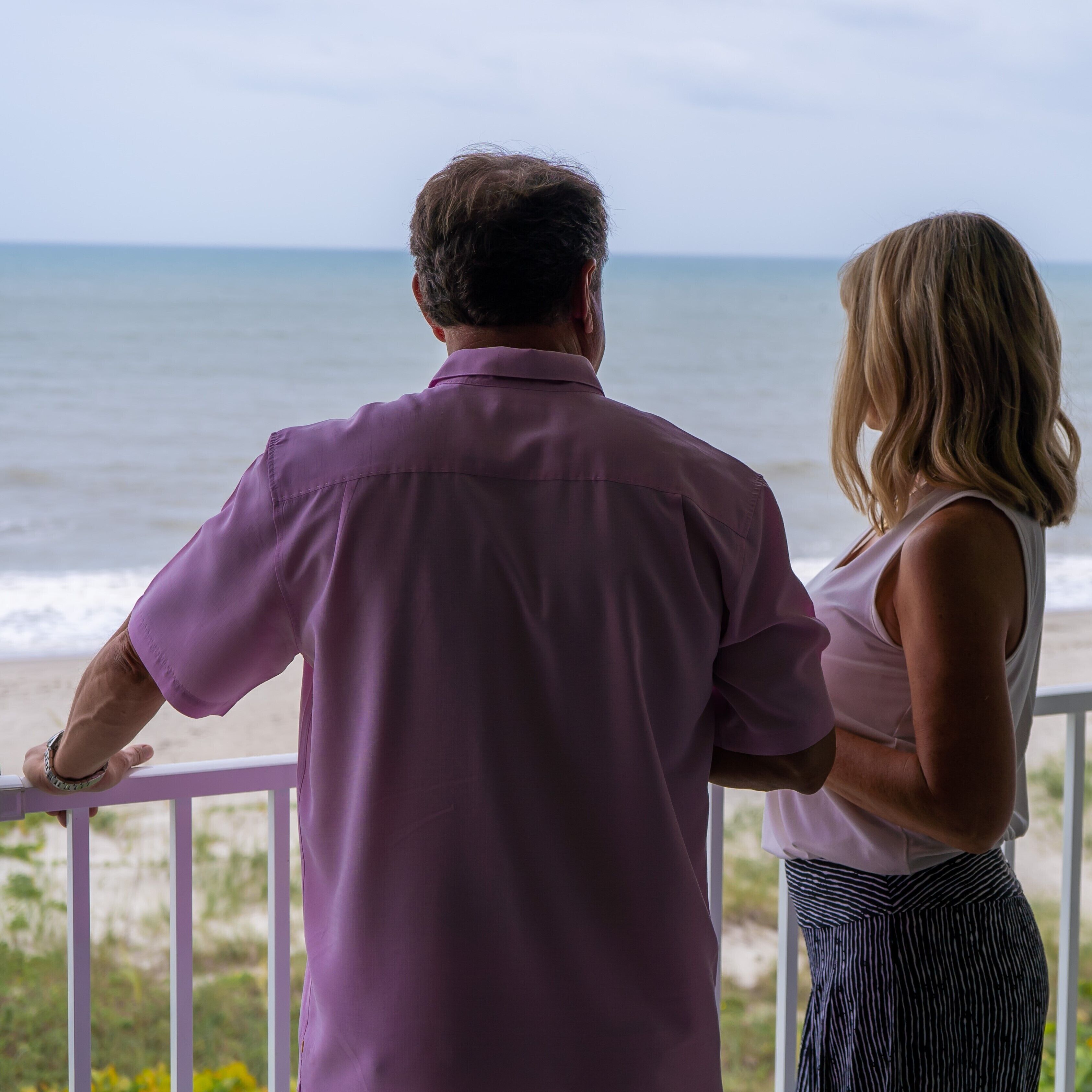 Um casal está em uma varanda com vista para uma praia.