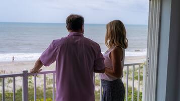 A couple standing on a balcony overlooking a beach.