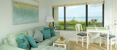 A living room with a sofa, chairs, a table, a lamp, and a view of the ocean.