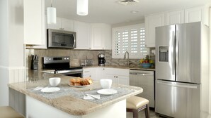 Una cocina moderna con armarios blancos, electrodomésticos de acero inoxidable, encimera de granito y una isla central con asientos.