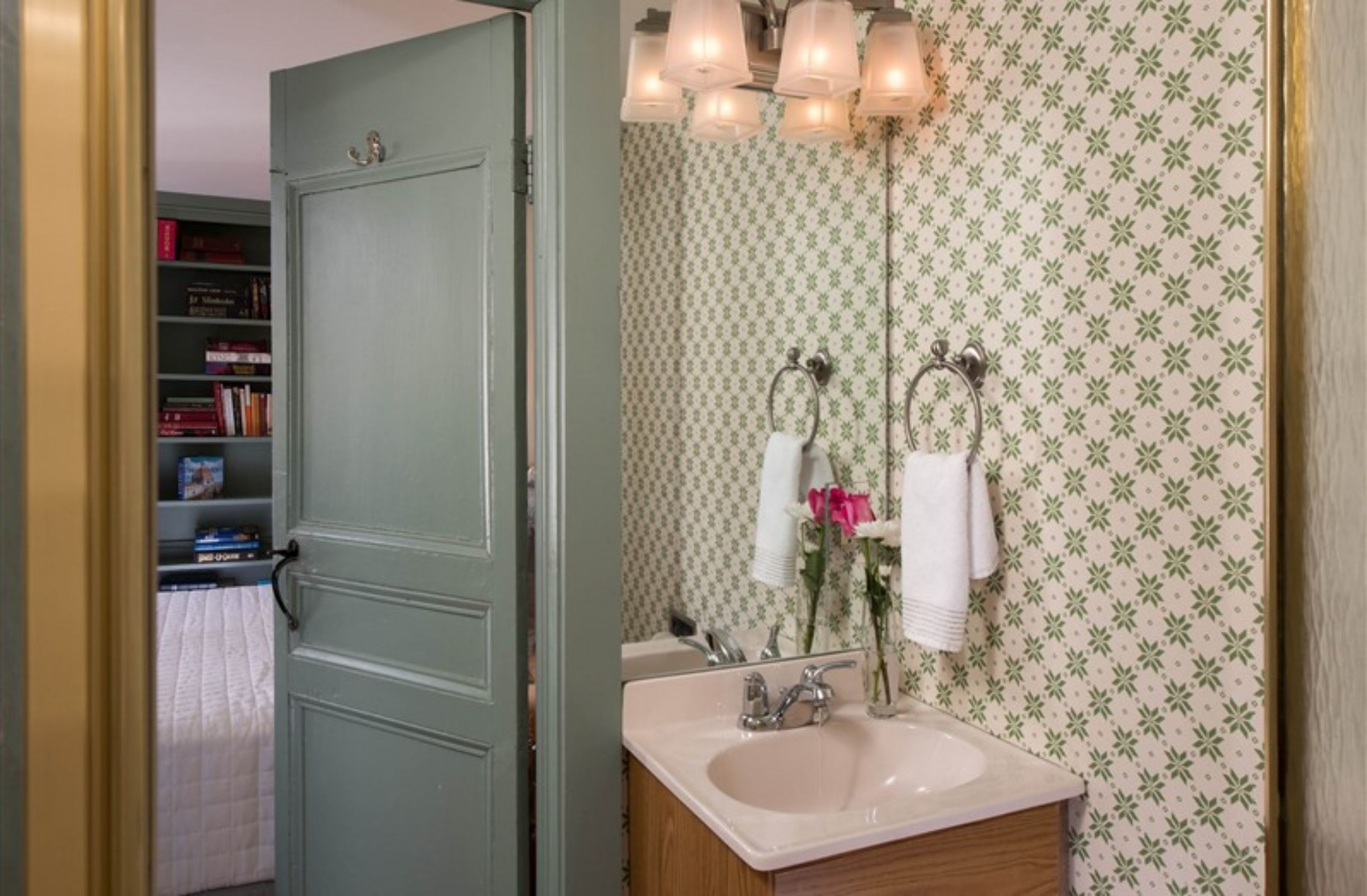 A bathroom with a sink, mirror, and towel rack. There is a door leading to a room with a bookshelf.