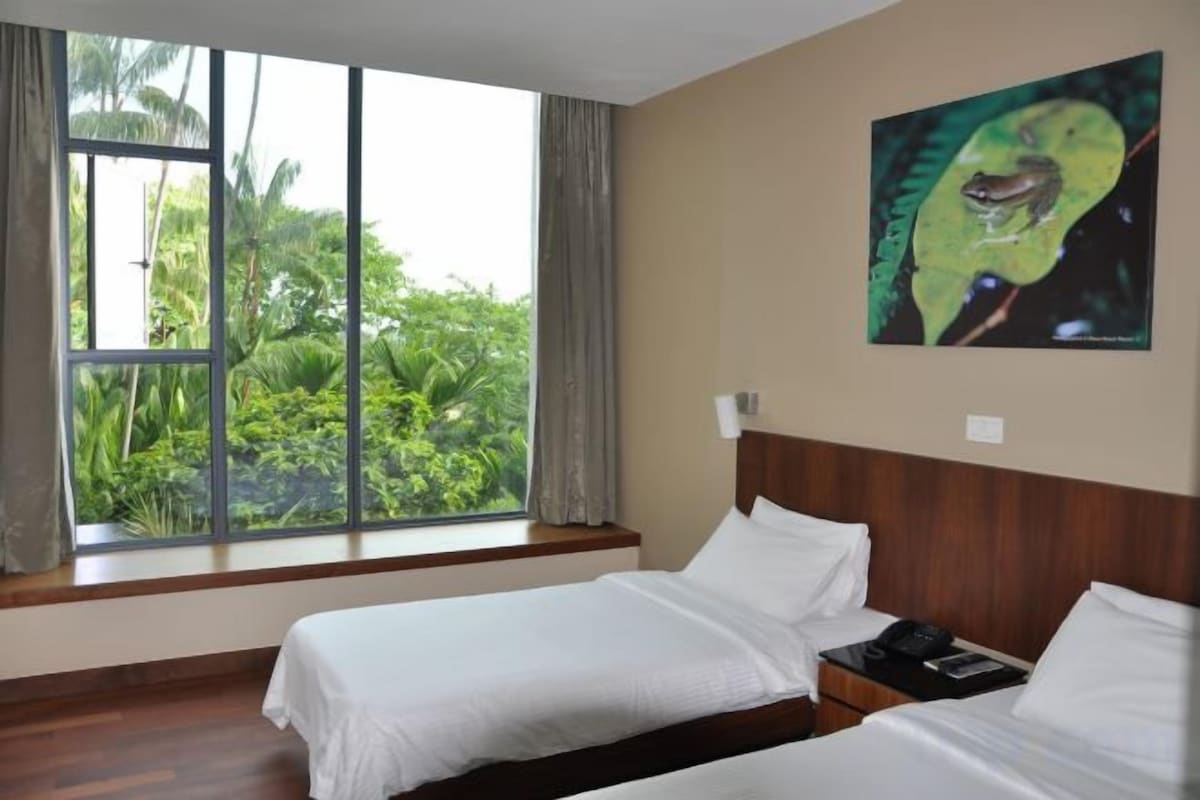 Een hotelkamer met twee bedden, een groot raam met gordijnen, een schilderij aan de muur en uitzicht op groen.