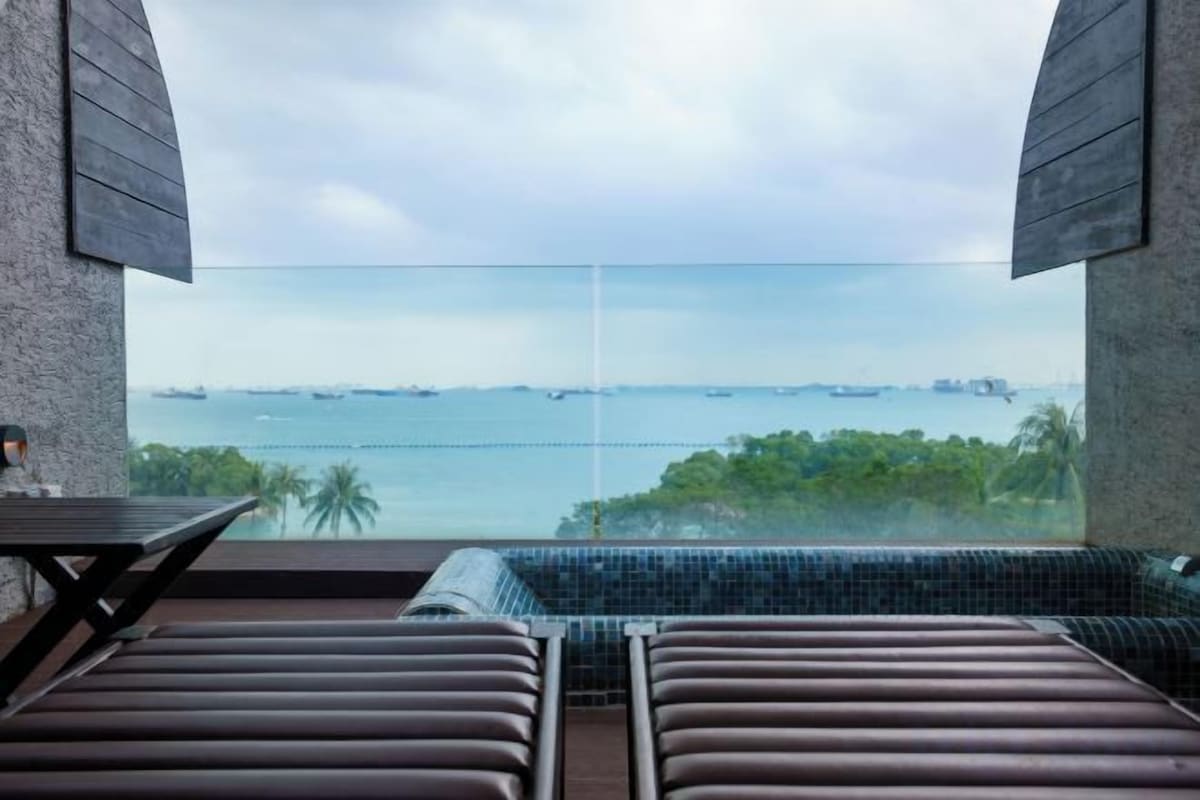 A balcony with a view of the sea, a glass partition, and a seating area with cushions.