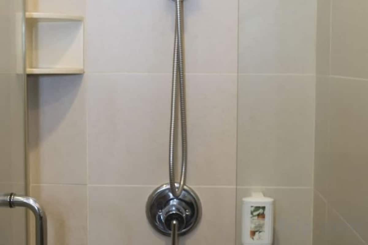 Une douche équipée d’un pommeau de douche amovible, d’un distributeur de savon et d’une petite étagère fixée au mur.