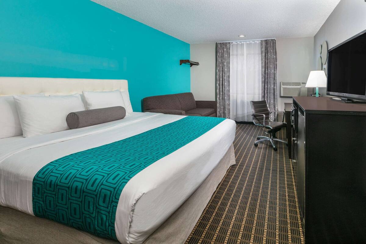 A hotel room with a large bed, a desk, a television, and a window with curtains.