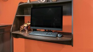 Un escritorio con computadora, monitor, teclado y ratón frente a una pared naranja.