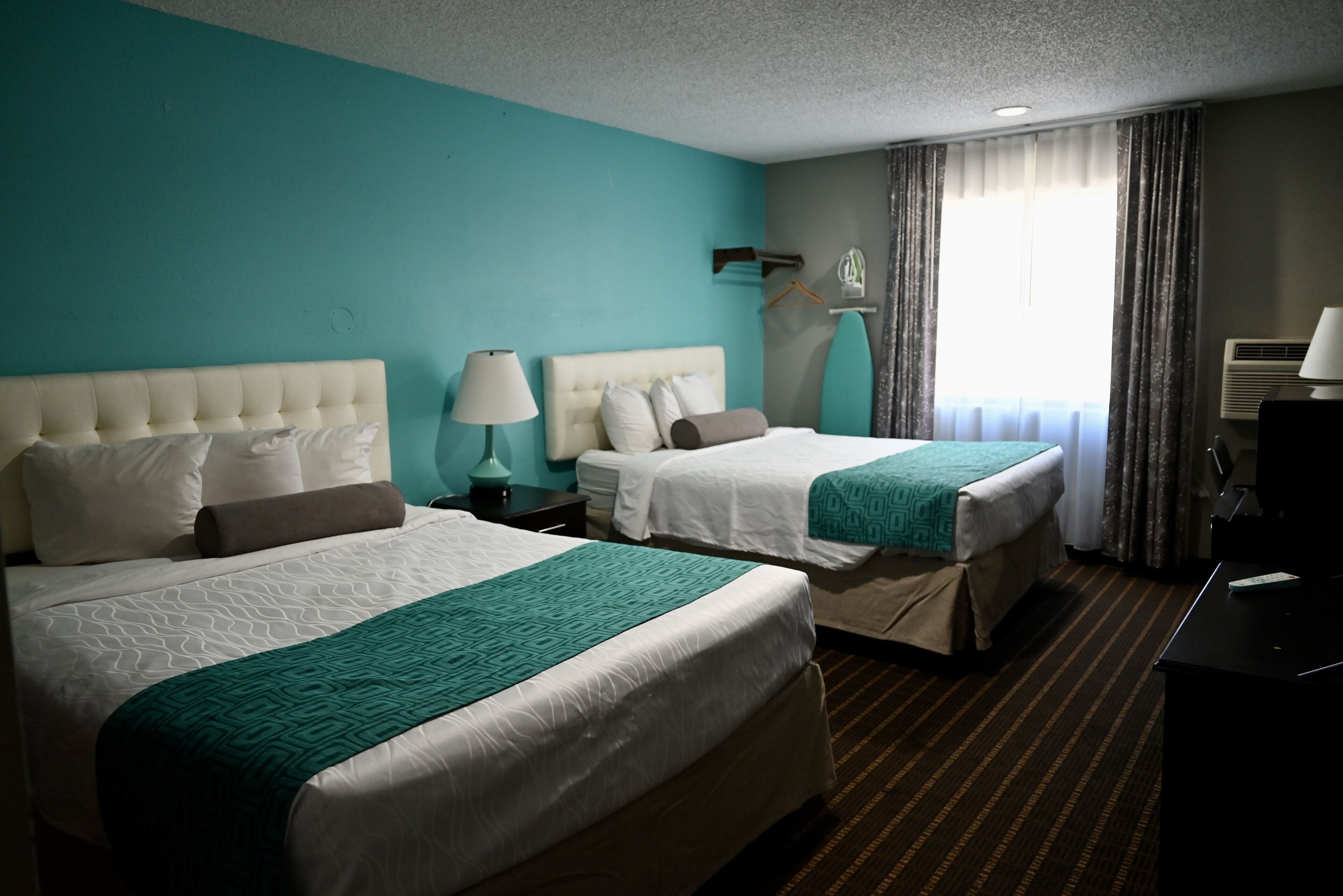 Une chambre d’hôtel avec deux lits, des murs de couleur turquoise et une moquette à rayures.