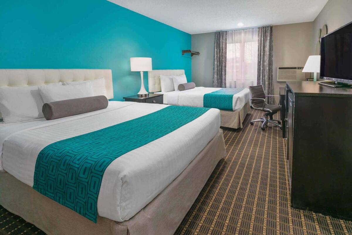 A hotel room with two beds, a desk, and a television.
