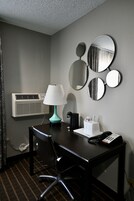 Habitación de hotel con escritorio, lámpara, teléfono, cafetera y aire acondicionado instalado en la pared.