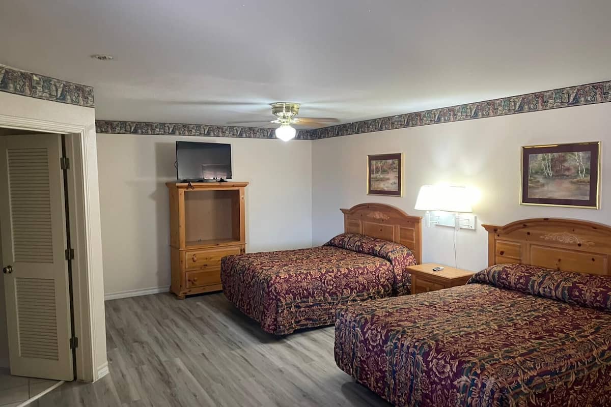 A hotel room with two beds, a TV on a wooden cabinet, a ceiling fan, and two framed pictures on the wall.