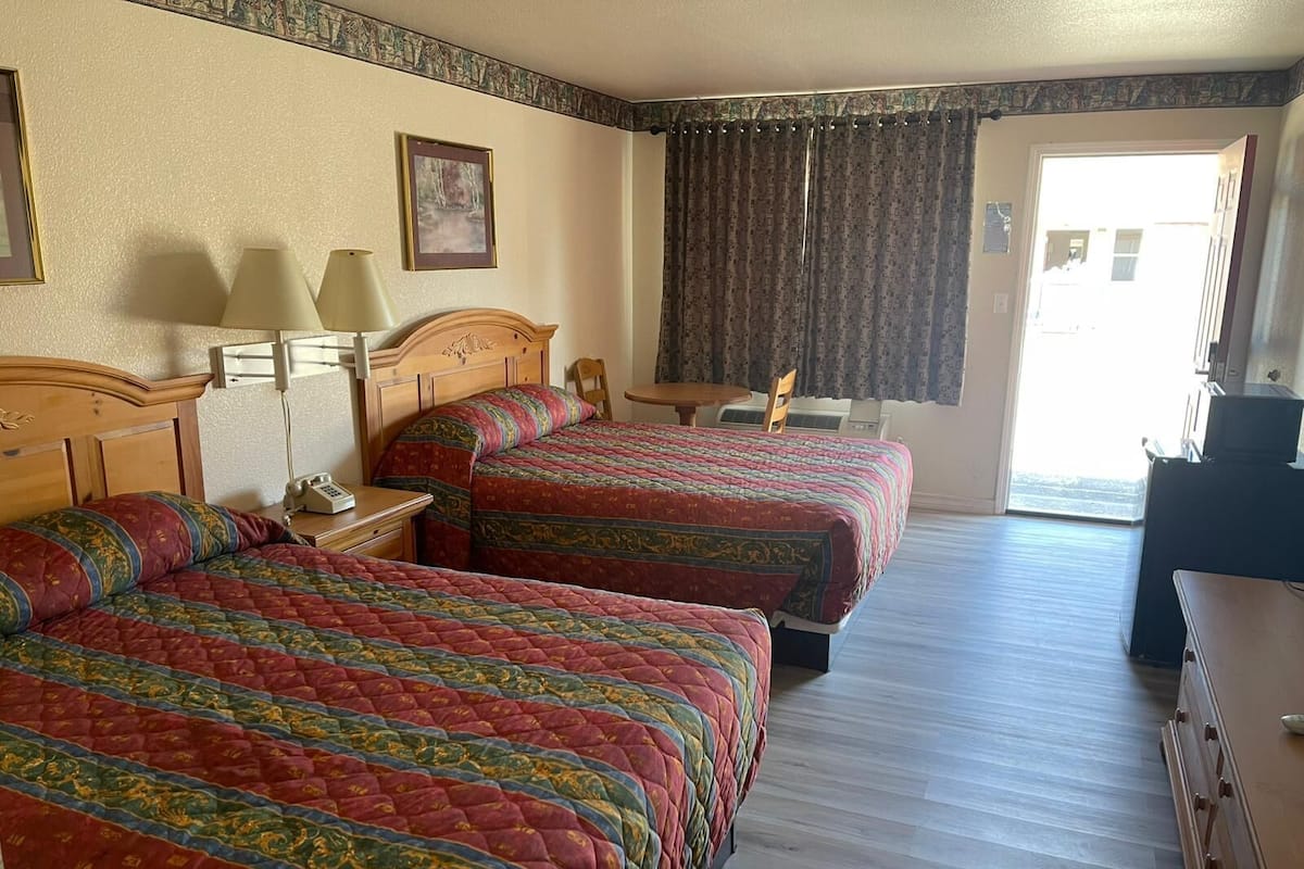 A hotel room with two beds, a desk, a chair, a lamp, and a window with curtains.