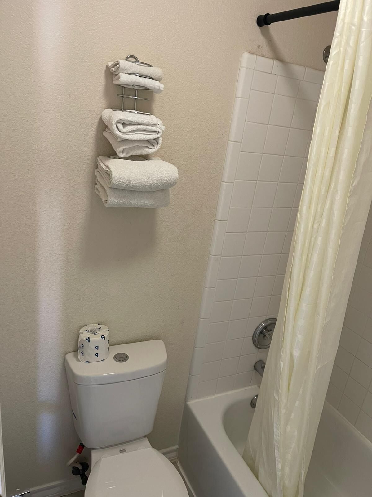 A bathroom with a toilet, a stack of white towels, a shower curtain, and a toilet paper holder.