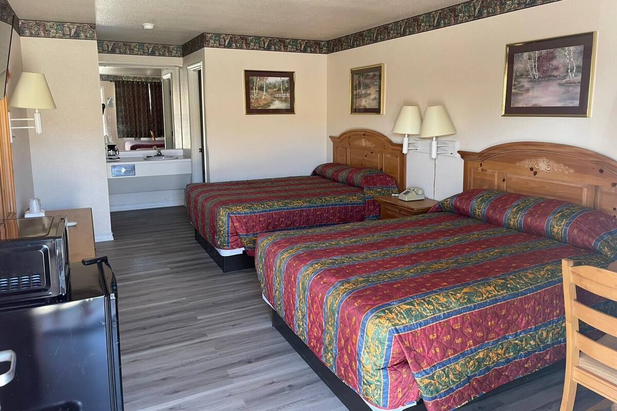 A hotel room with two beds, a desk, and a refrigerator.