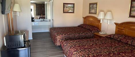 Habitación de hotel con dos camas, un escritorio, un televisor y un baño visible a través de una puerta abierta.
