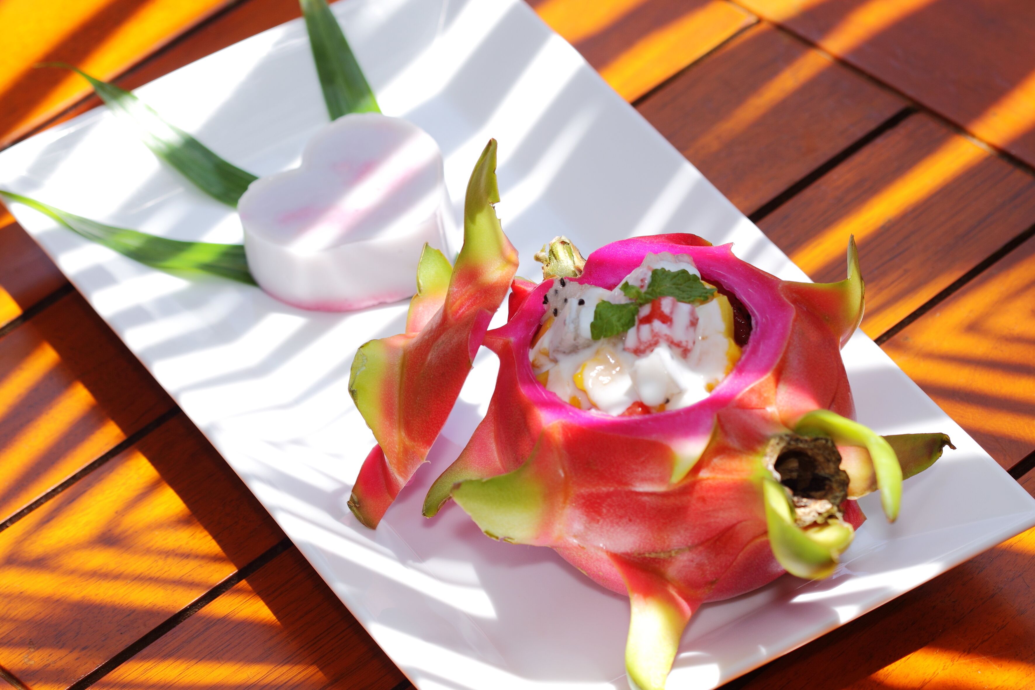 A white plate with a dragon fruit and a small bowl of what appears to be a creamy dessert, placed on a wooden table.