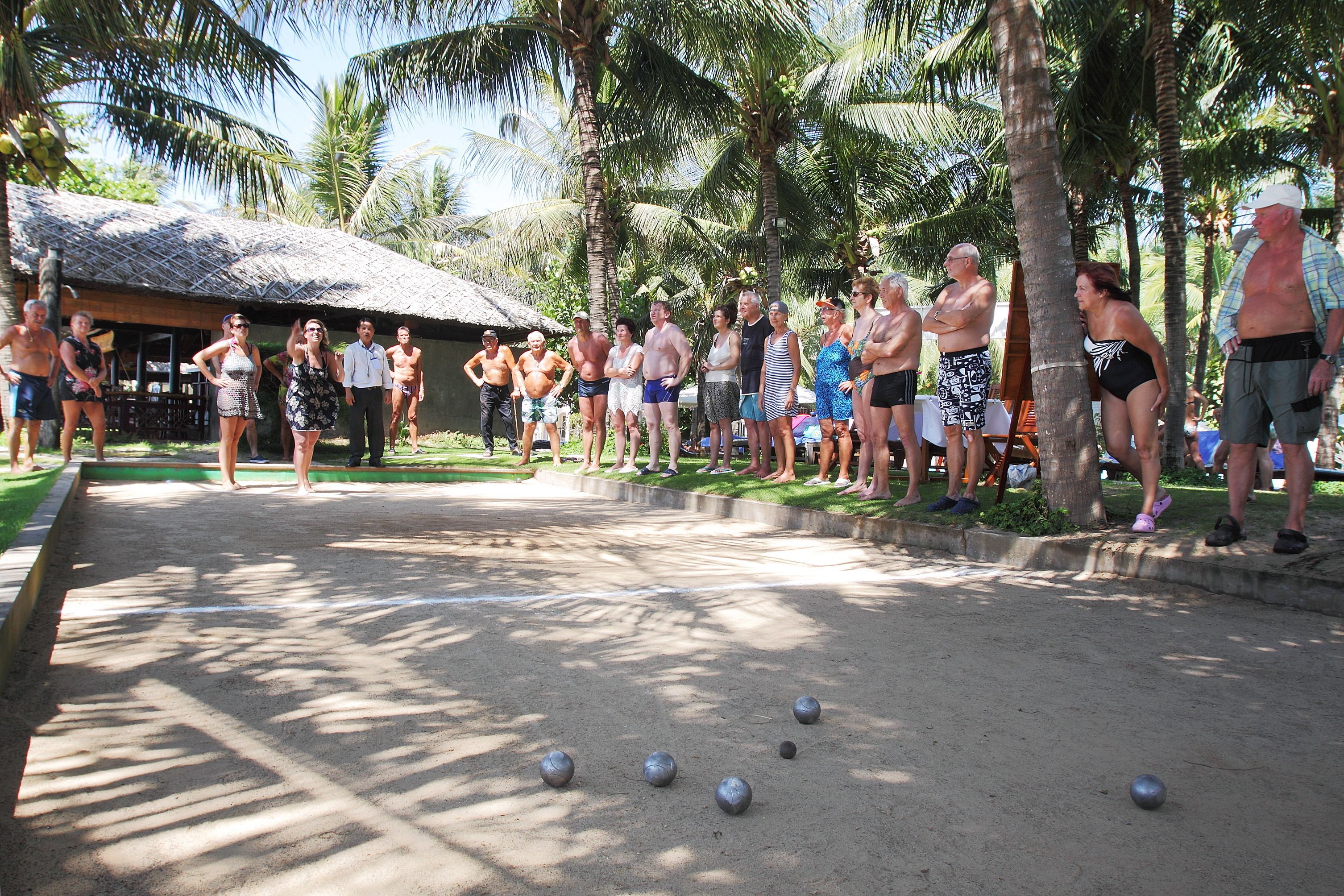 A group of people playing a game outdoors with a thatched-roof building in the background.