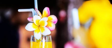 A cocktail glass with a layered drink, a straw, and a flower garnish on a bar counter.
