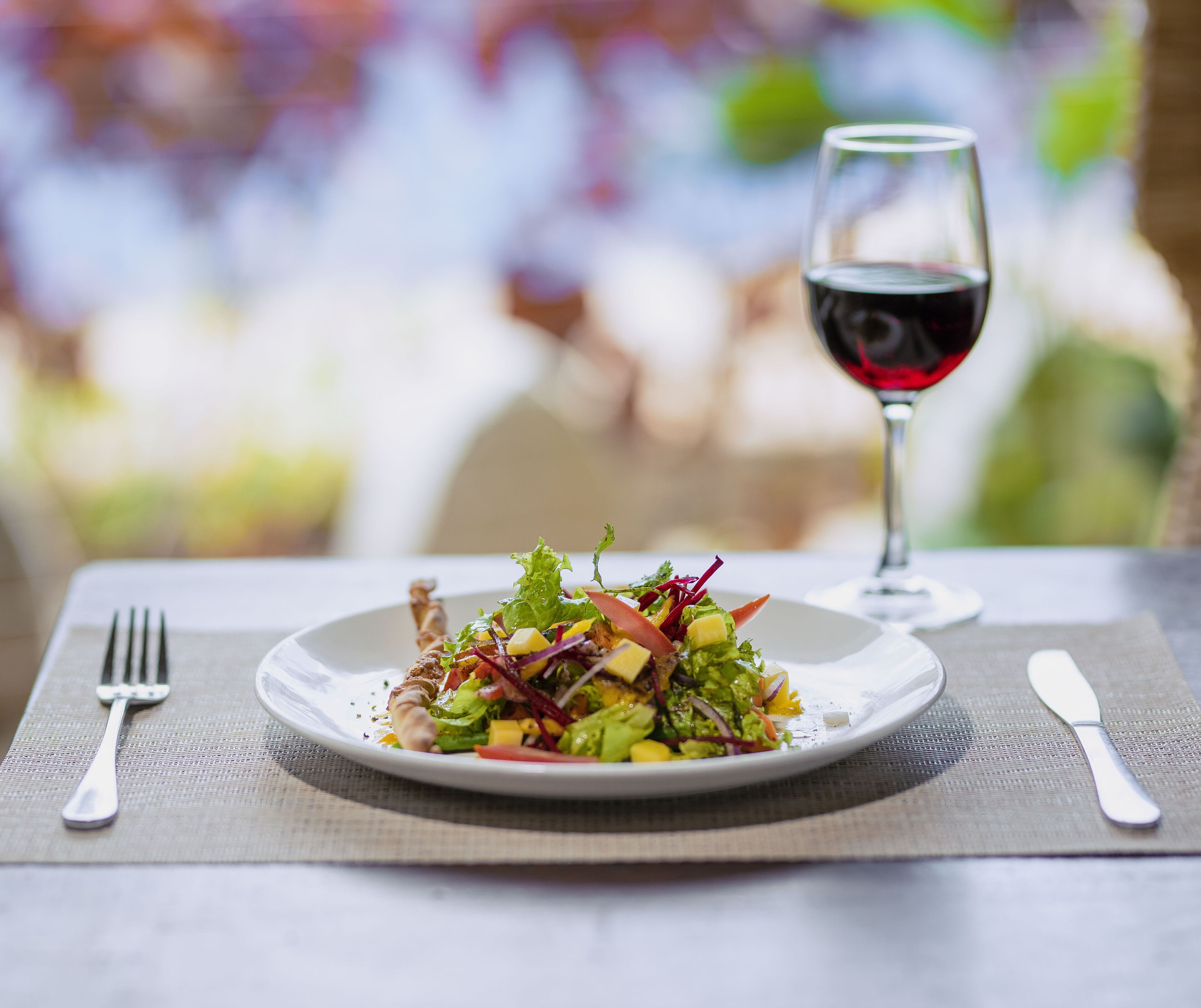 A plate of salad with a glass of red wine on a table.