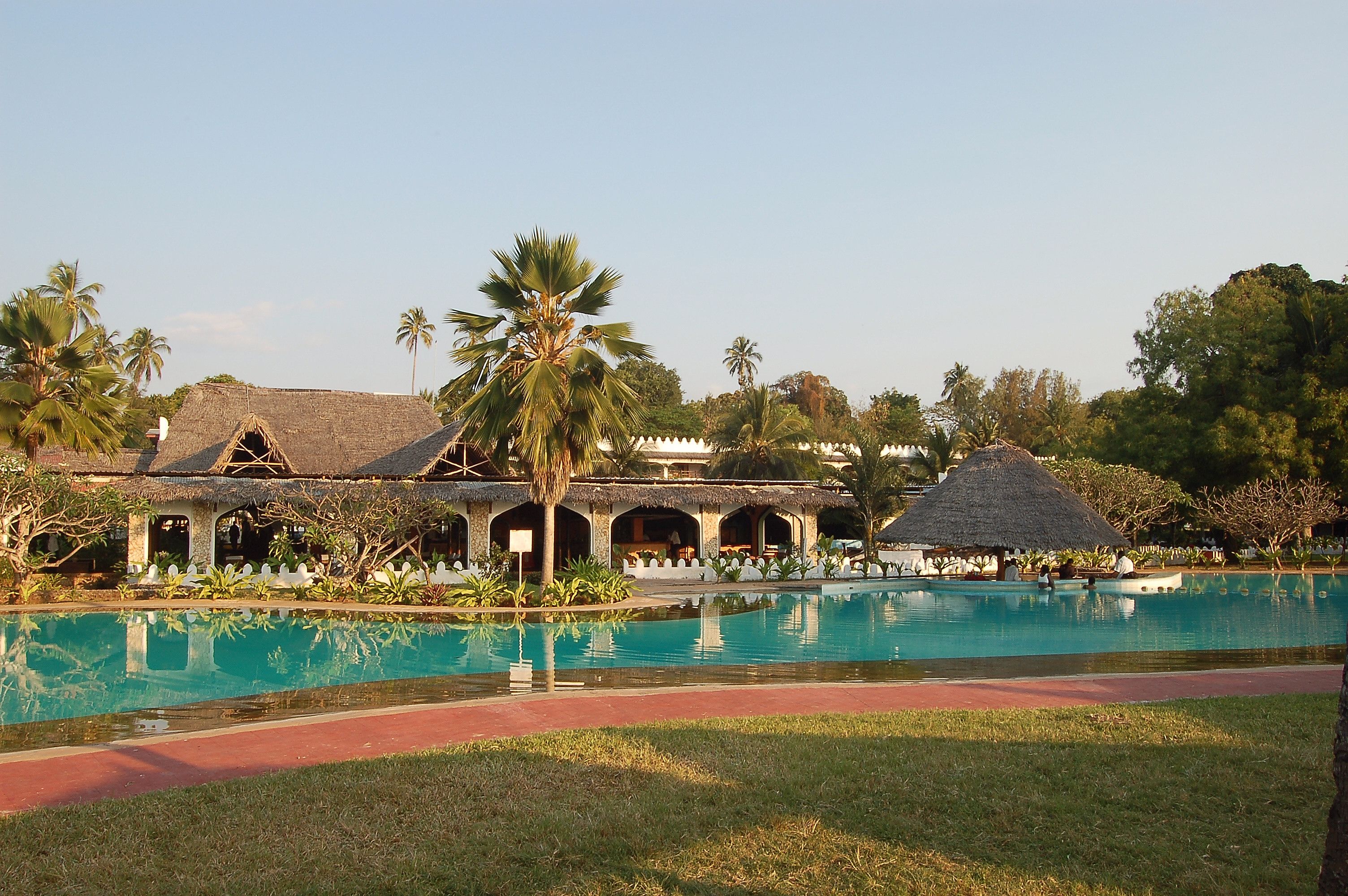 A resort with a swimming pool, thatched-roof structures, and palm trees.