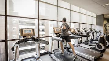 A gym with treadmills and exercise equipment, large windows, and a view of the city.