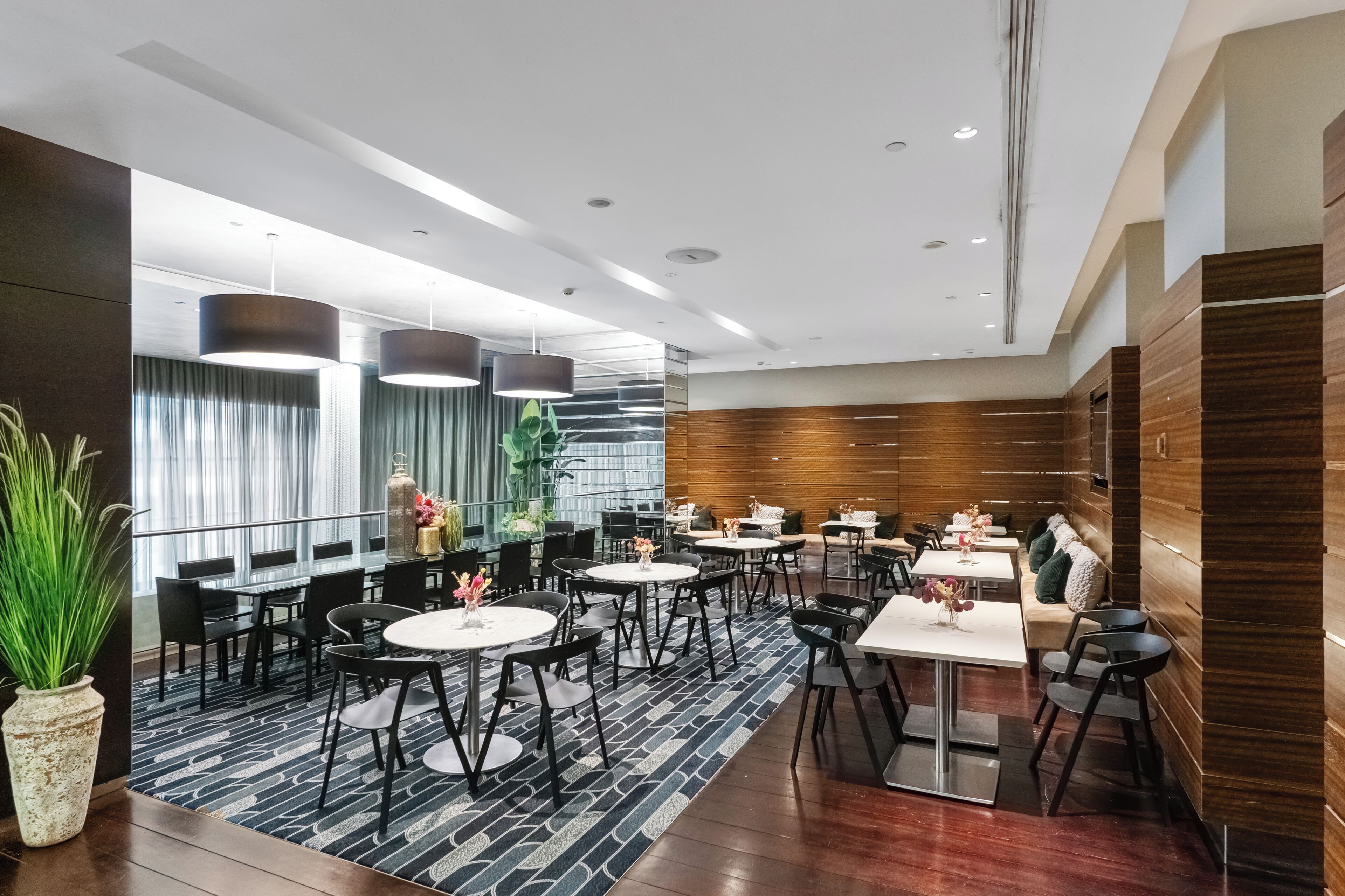 Una hall moderna di un hotel con tavoli rotondi, sedie nere e una moquette decorata.