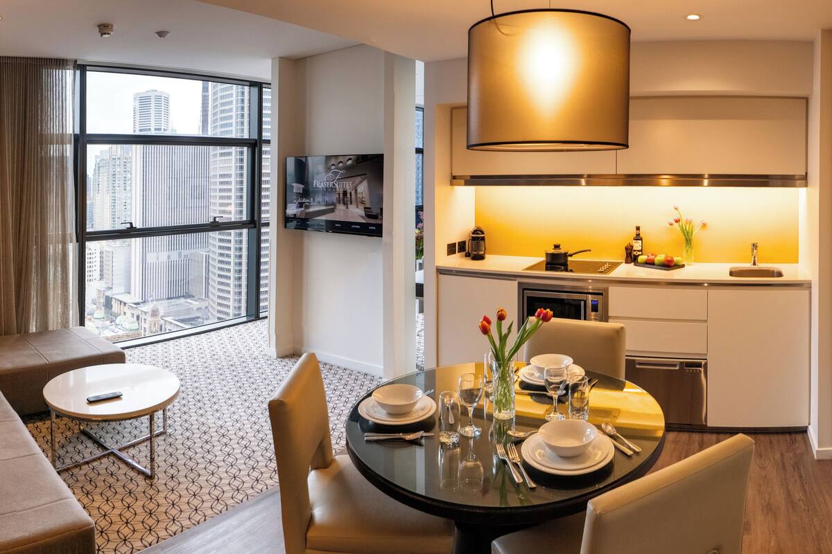 A modern hotel room with a living area, dining space, and kitchenette.