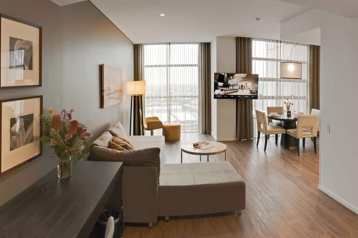 A modern hotel room with a living area, dining space, and a large window with curtains.