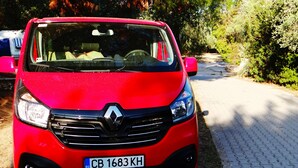 Une voiture Renault rouge est garée sur une route asphaltée, avec des arbres et de la végétation en arrière-plan.