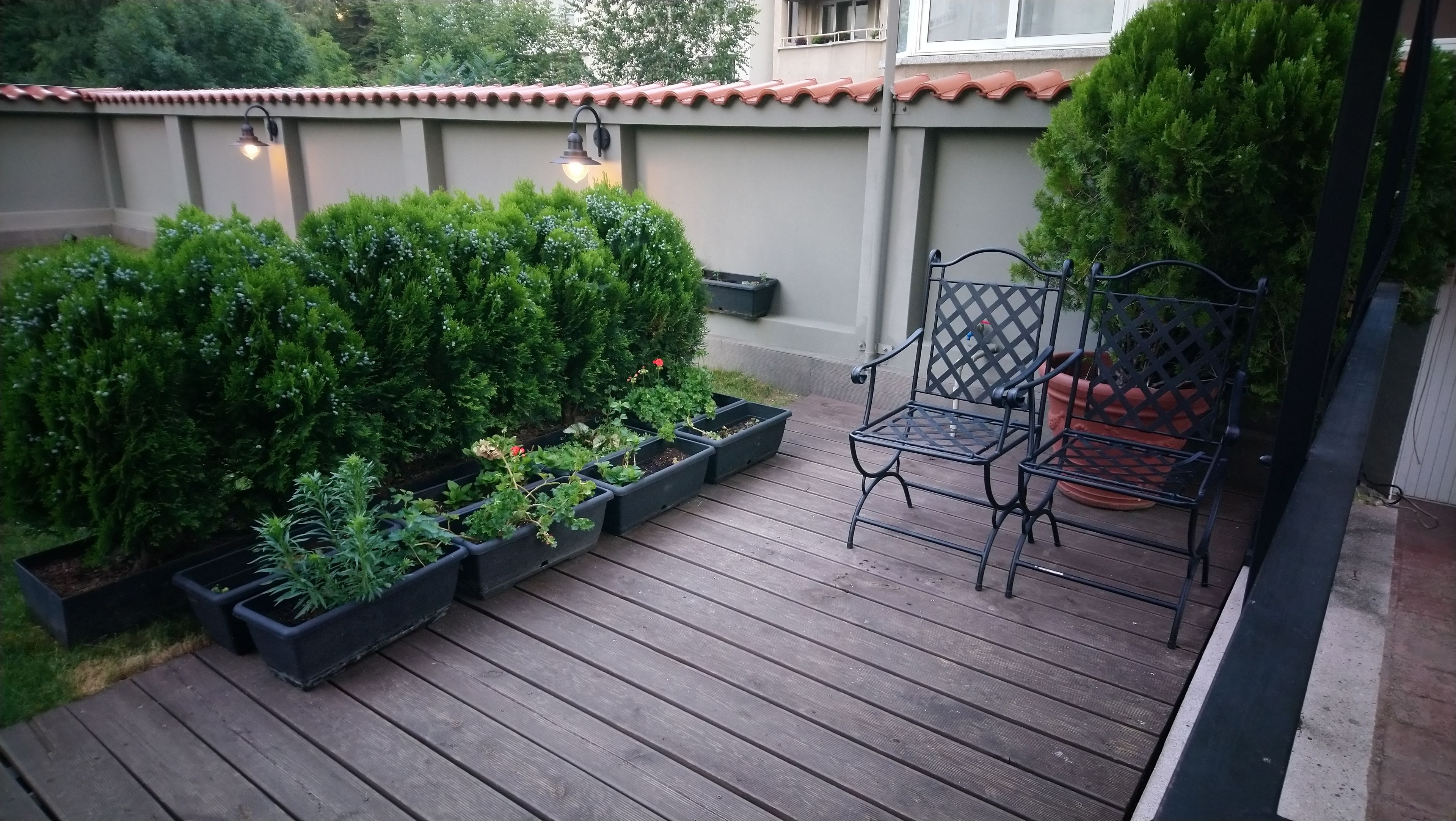 A wooden deck with potted plants and a metal chair.