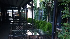 Une terrasse extérieure avec des tables et des chaises en métal, un espace abrité et de la verdure.