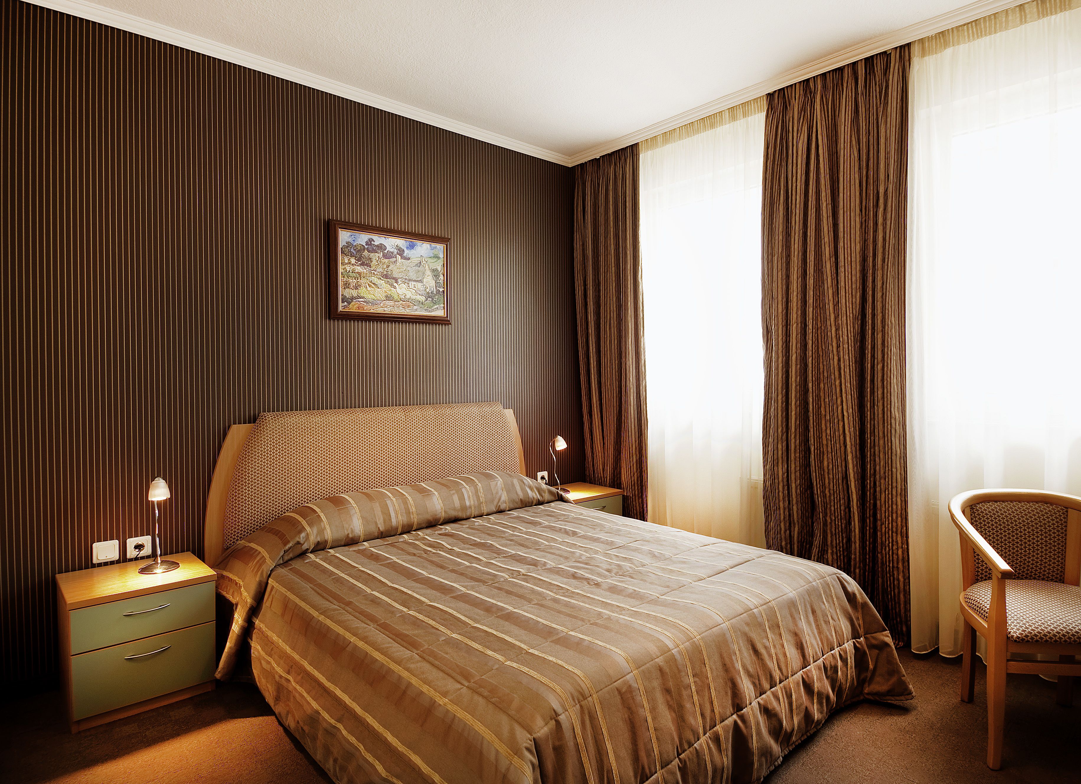 Een hotelkamer met een groot bed, een nachtkastje, een stoel en een schilderij aan de muur.