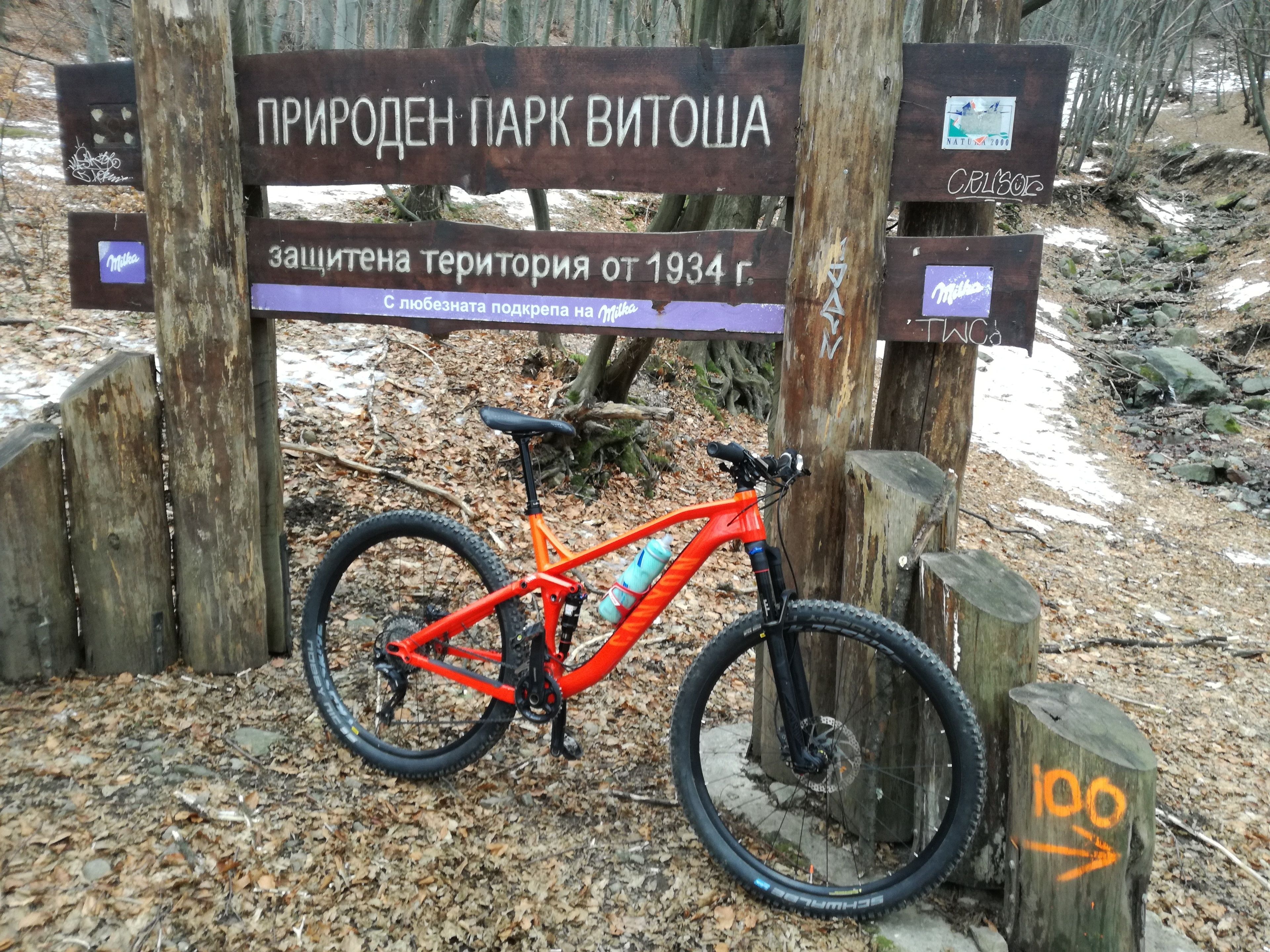 A wooden sign with text in a foreign language, a bicycle, and a natural outdoor setting.
