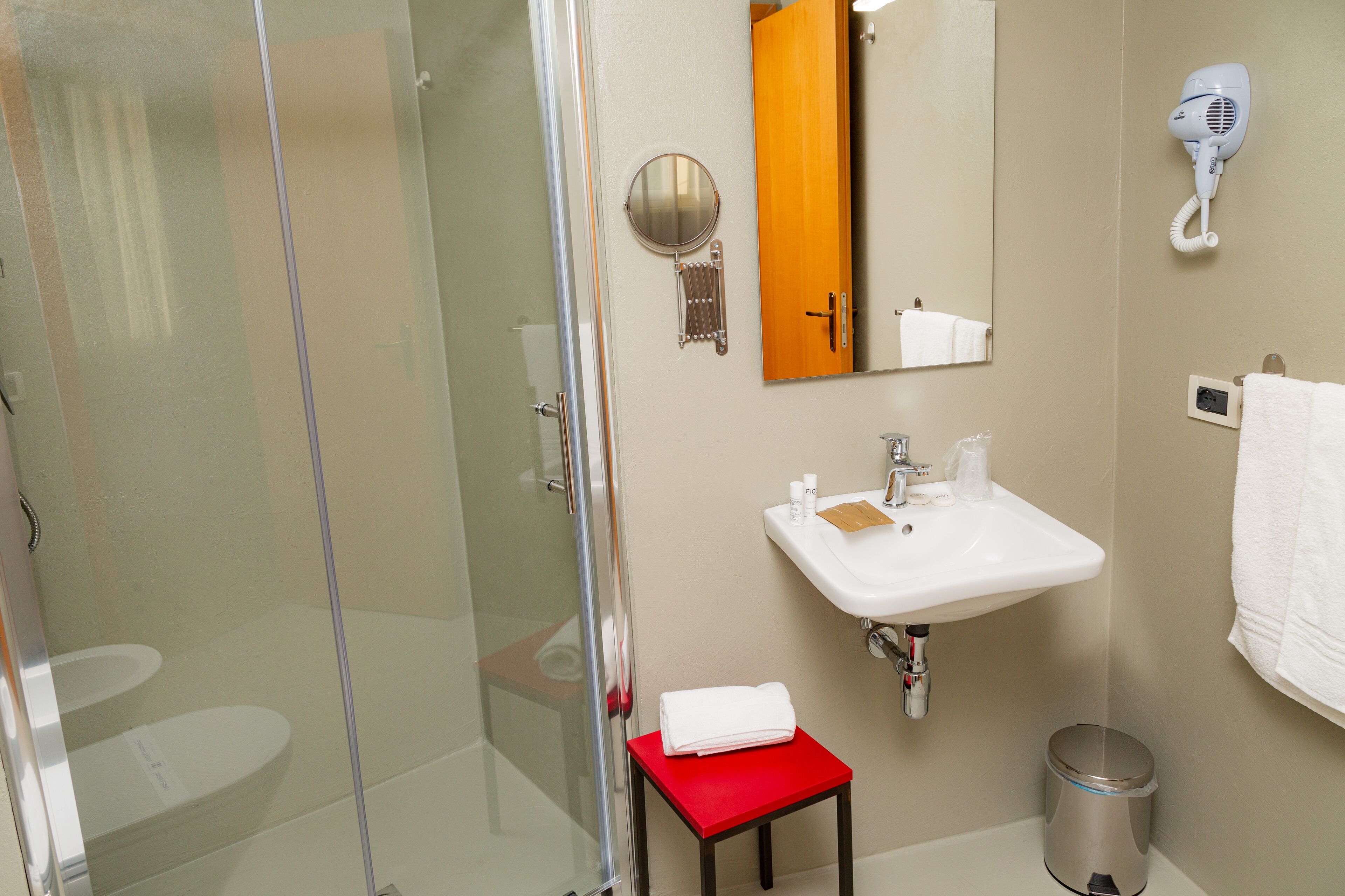Een badkamer met een glazen douchecabine, een wastafel met spiegel erboven en een föhn aan de muur bevestigd.