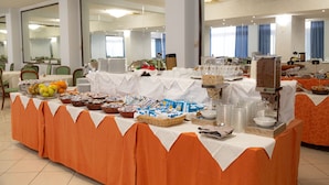 Montaje de bufé con diferentes alimentos y bebidas, incluyendo frutas, aperitivos y una estación de café.