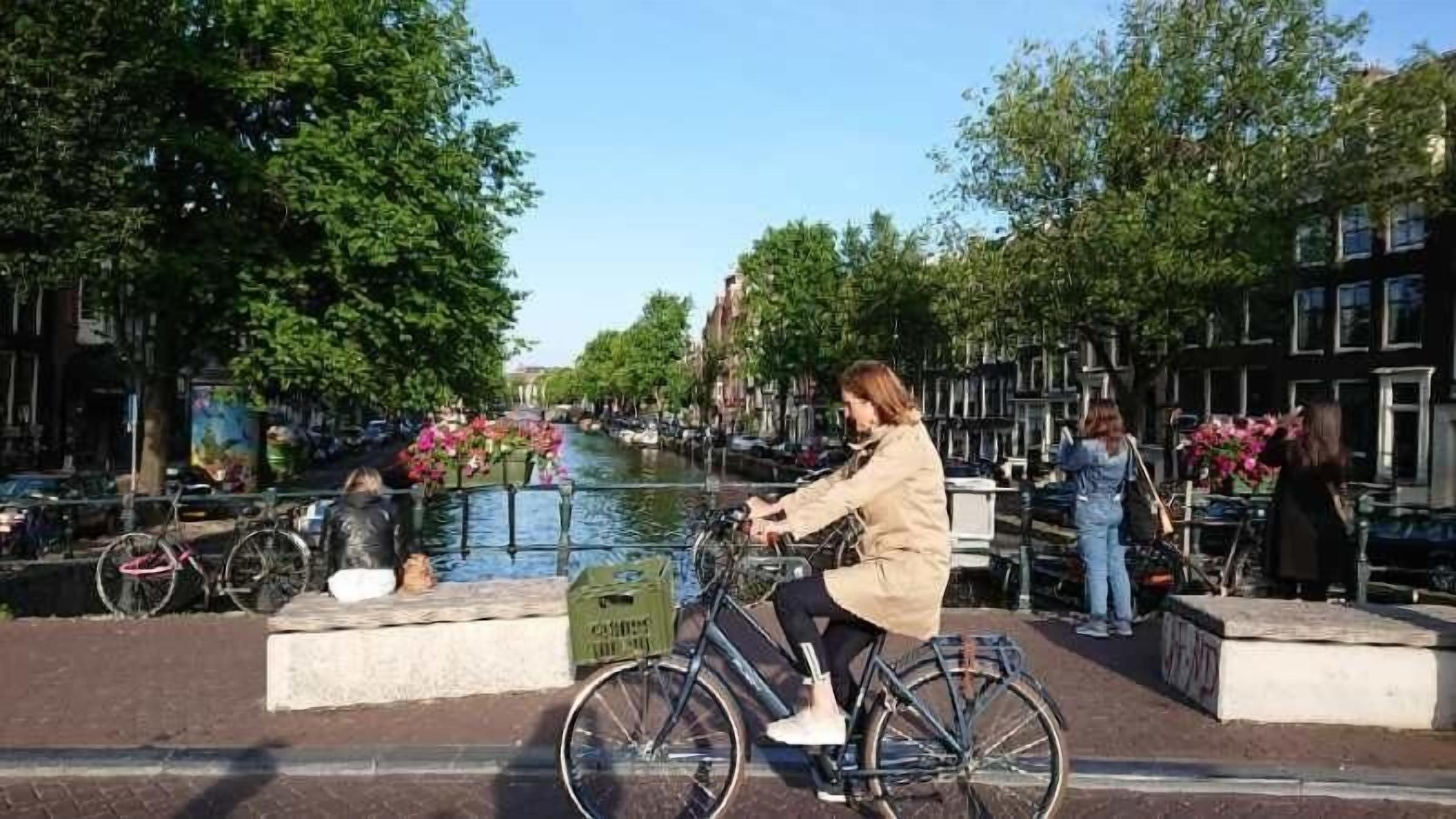 A canal-side bike path with a cyclist, trees, and buildings in the background.