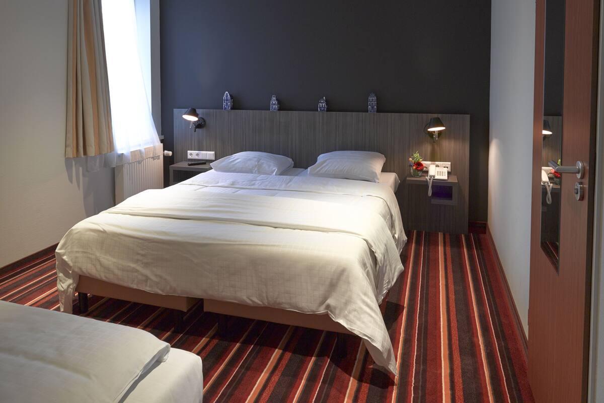 Quarto de hotel com uma cama grande, uma mesa de cabeceira com abajur, telefone e um pequeno objeto decorativo na parede.