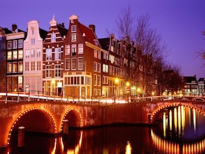 A historic bridge with illuminated arches over a canal, reflecting the buildings on the opposite bank.