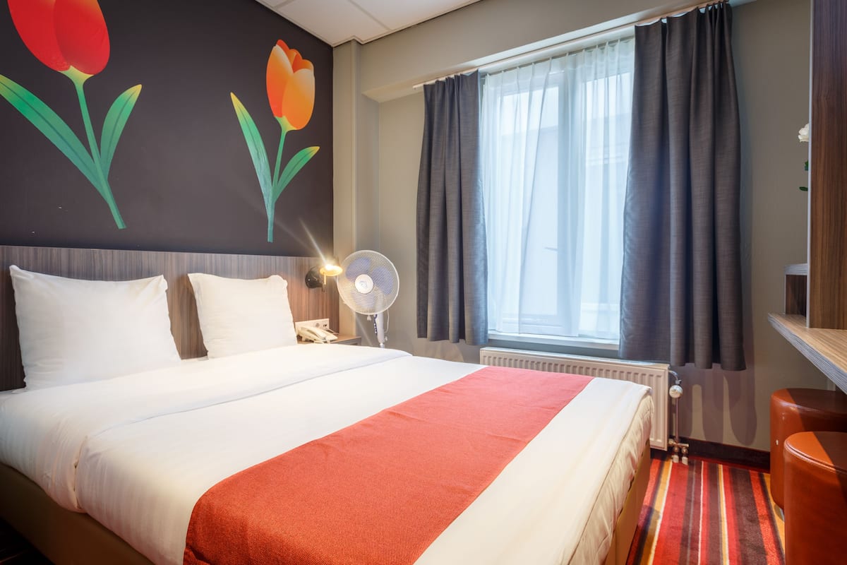 Quarto de hotel com cama grande, mesa de cabeceira, ventoinha e janela com cortinas.