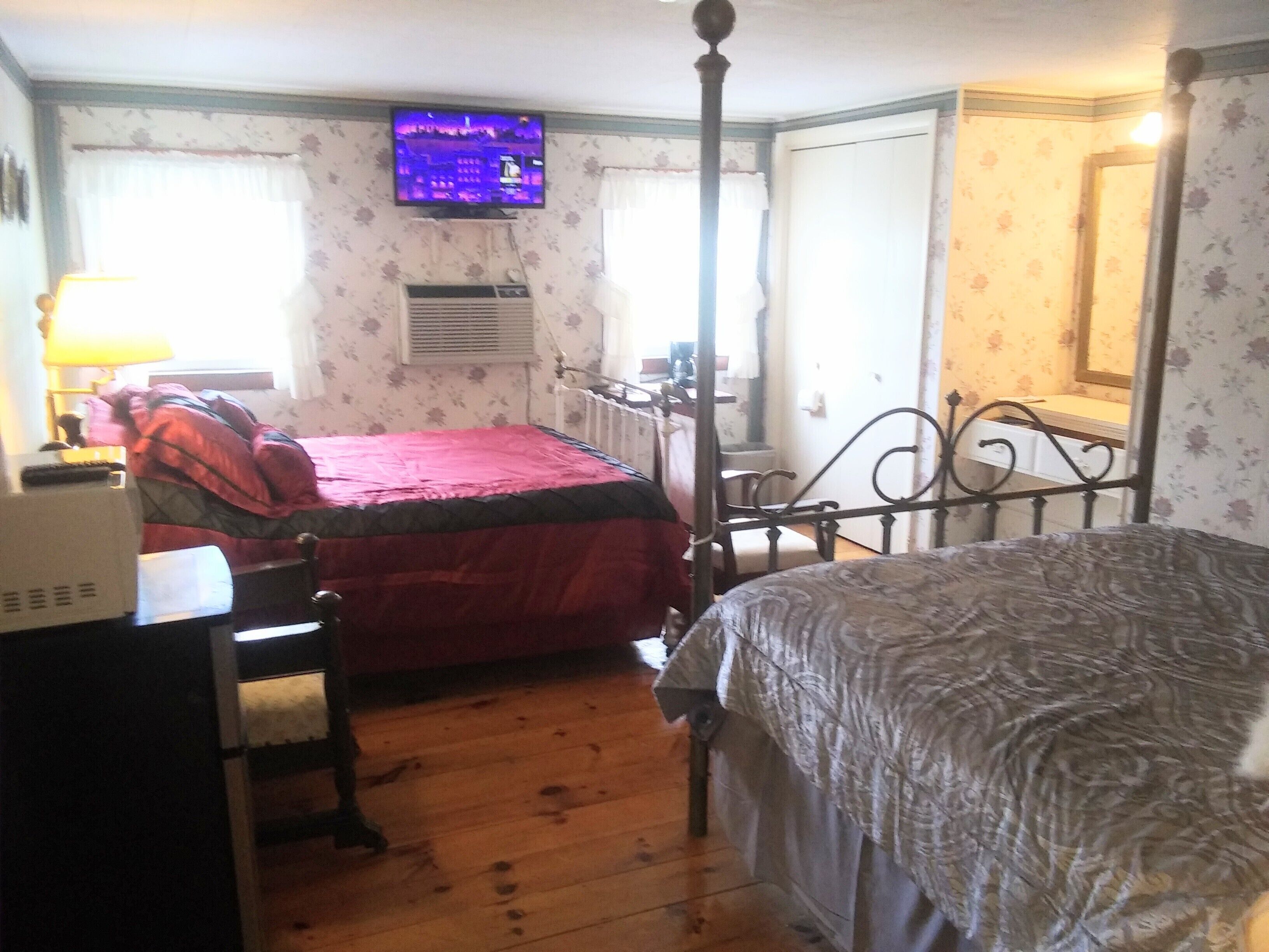 Une chambre avec deux lits, un téléviseur fixé au mur, un radiateur et un bureau avec une lampe.