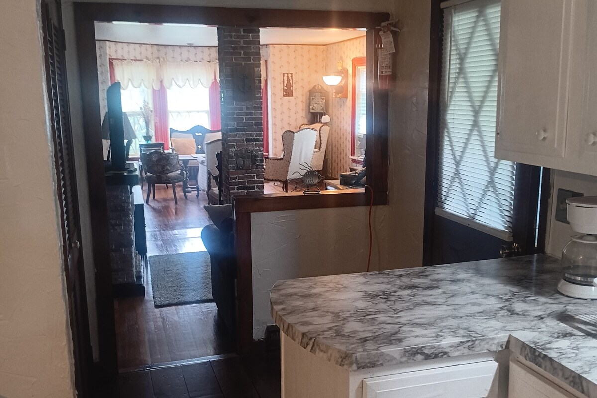 A kitchen with a marble countertop, a white refrigerator, and a wooden dining table with chairs.