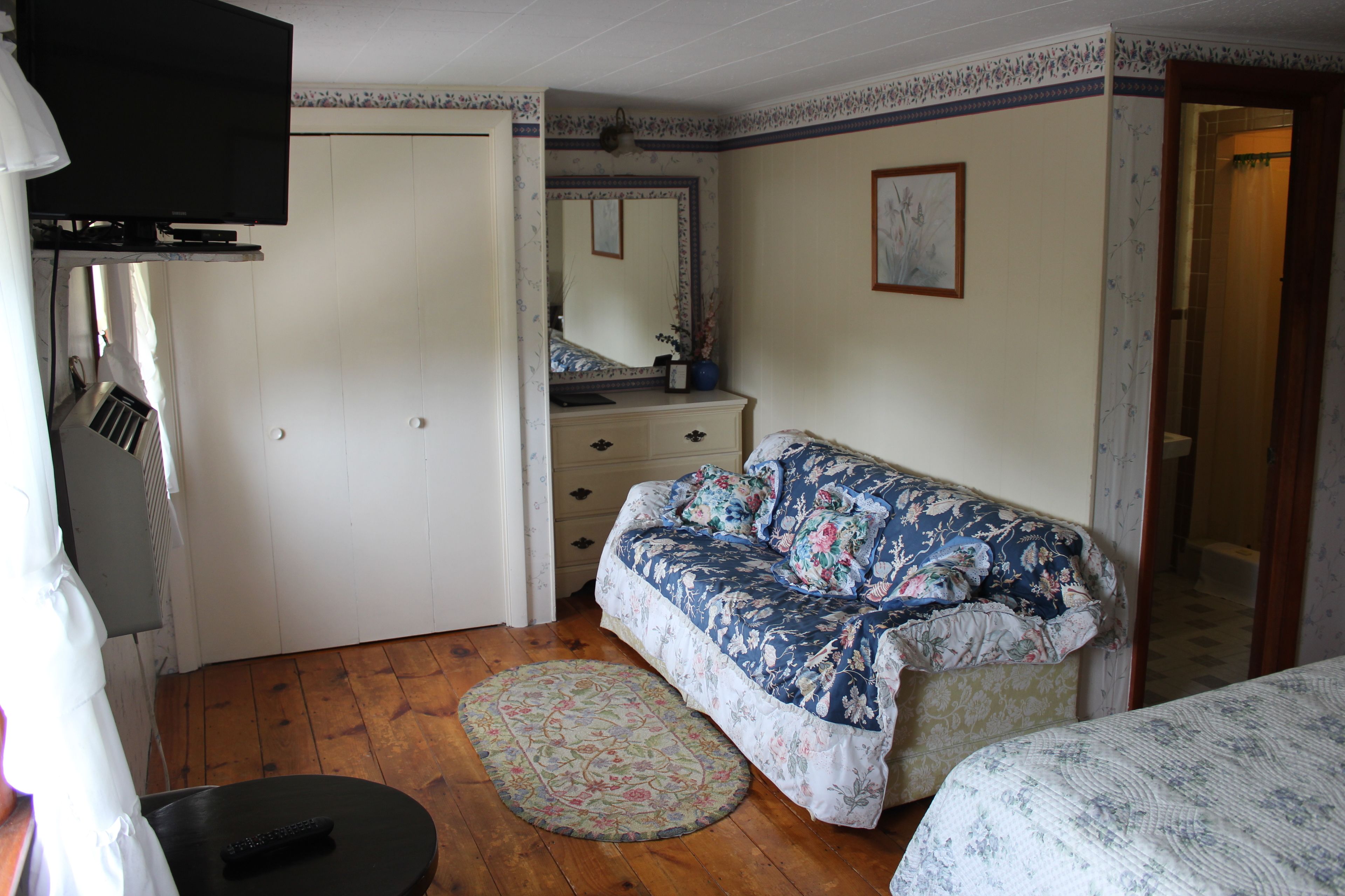 Een slaapkamer met een bank met bloemenprint, een rond tapijt, een dressoir en een aan de muur bevestigde televisie.