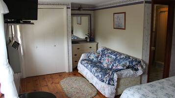Een slaapkamer met een bank met bloemenprint, een rond tapijt, een dressoir en een aan de muur bevestigde televisie.