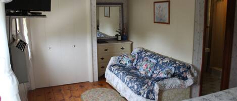 A bedroom with a floral-patterned sofa, a round rug, a dresser, and a television mounted on the wall.