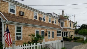 A two-story wooden house with a white picket fence, an American flag, and a sign indicating a business on the ground floor. - Sea Breeze Inn (Hyannis)