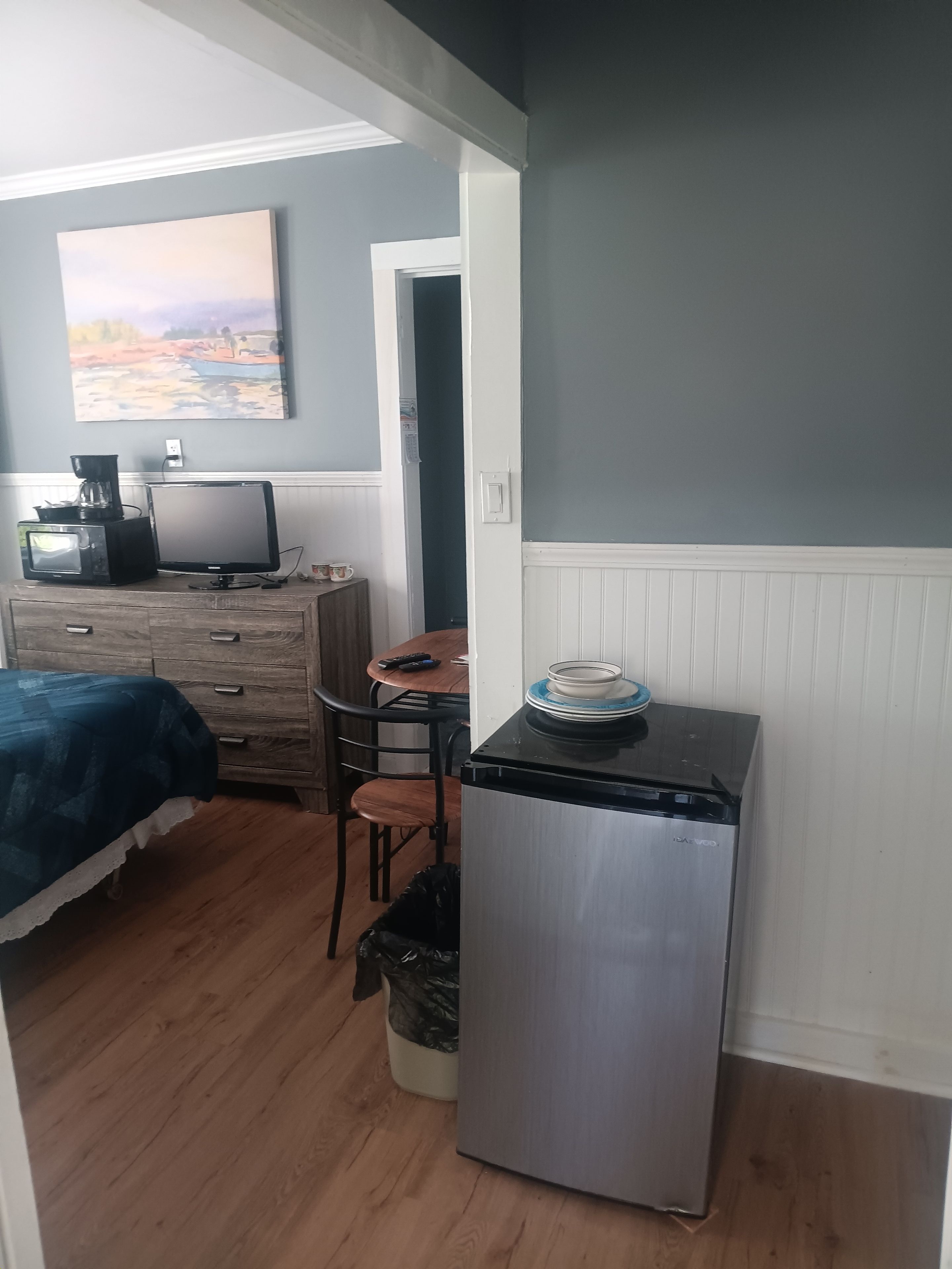 Ein kleines Zimmer mit einem Bett, einem kleinen Tisch, einem Kühlschrank und einem Bild an der Wand.