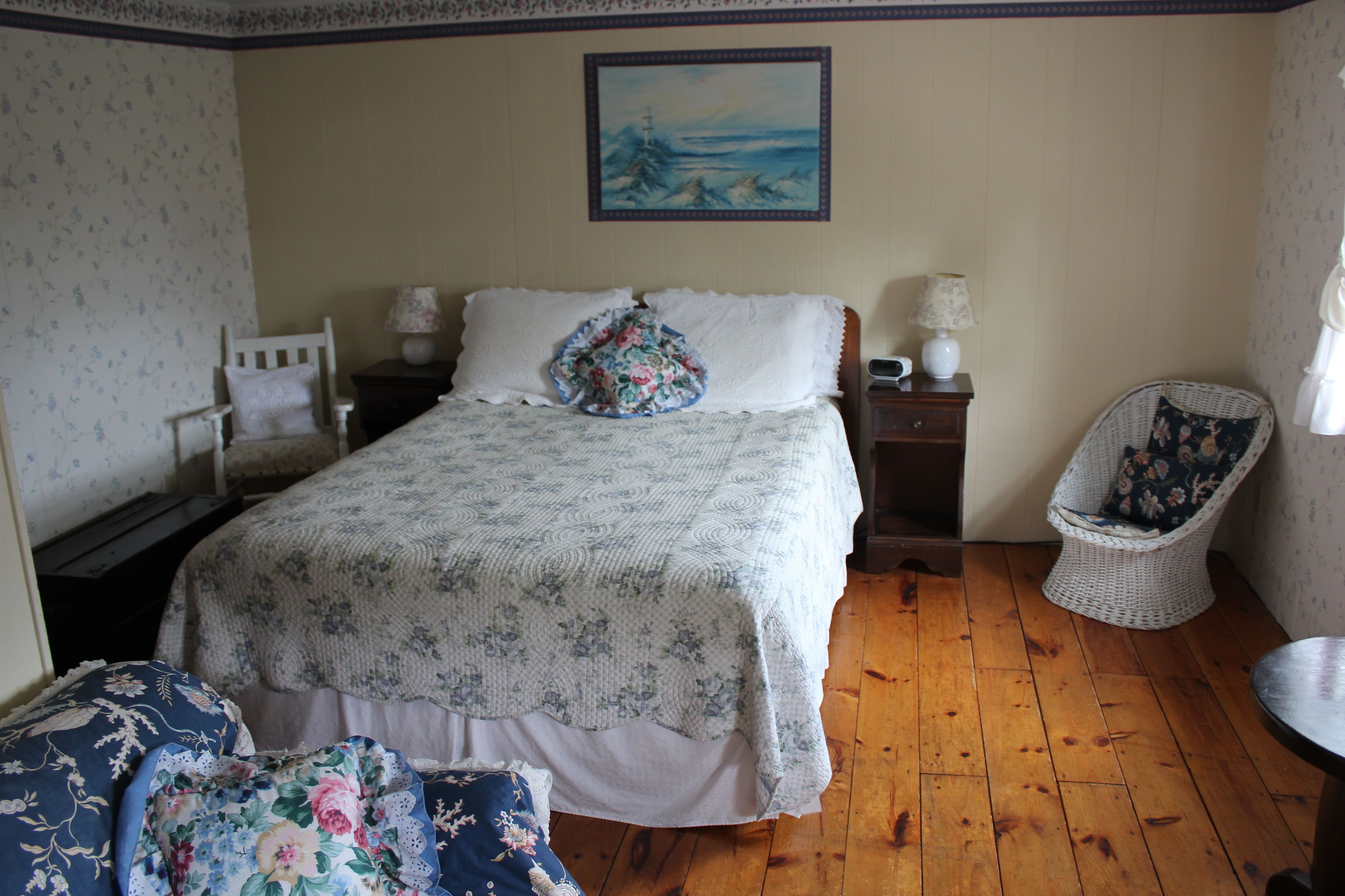 A bedroom with a bed, a chair, a nightstand, and a painting on the wall.