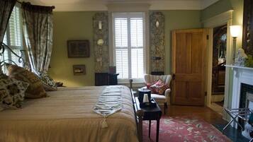 A bedroom with a large bed, a chair, a fireplace, and a window with curtains.